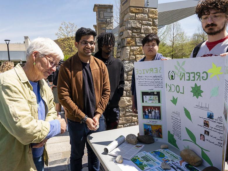 A visitor reviews a sustainability-themed poster project presented by two students.